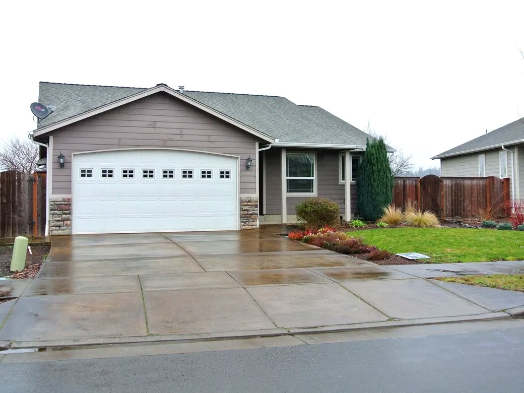 The front of the FETI Group Home house: a single-story gray home with a white garage door, a lawn and a fenced yard